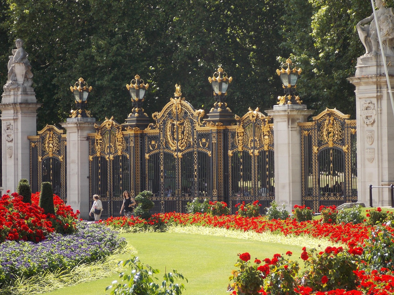 Ornate black and gold iron gates behind beds of red flowers
