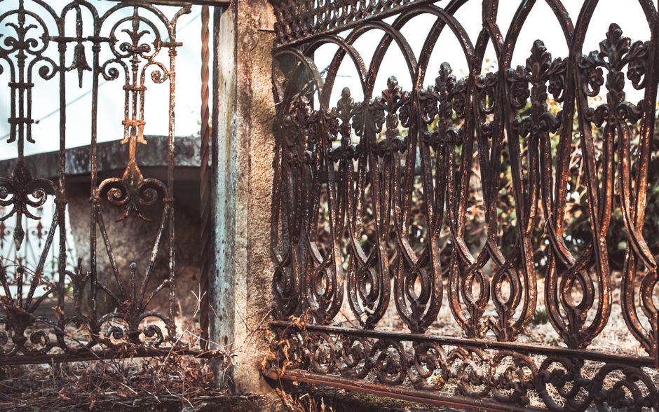Rust-streaked ornamental iron fence panels with scrollwork beside a concrete post.
