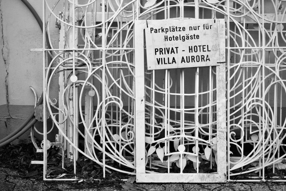 White scrolled iron gate panels with a hand lettered sign hung on the frame, in black and white.