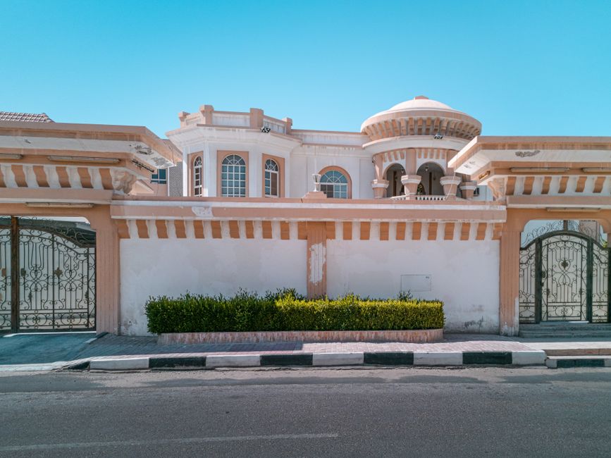Two arched wrought iron driveway gates set in a light plaster wall in front of a domed house.
