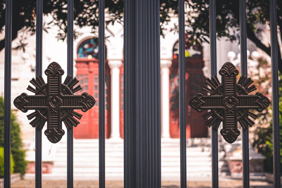 Dark metal gate bars with two cross shaped ornaments in front of a church entrance.