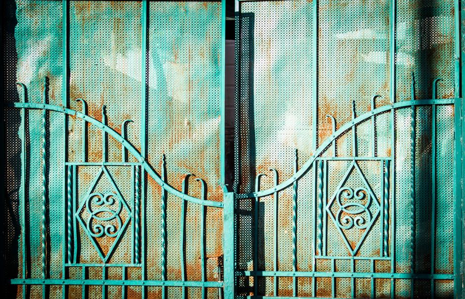 Teal painted iron gate with perforated panels, diamond scroll patterns and rust staining.